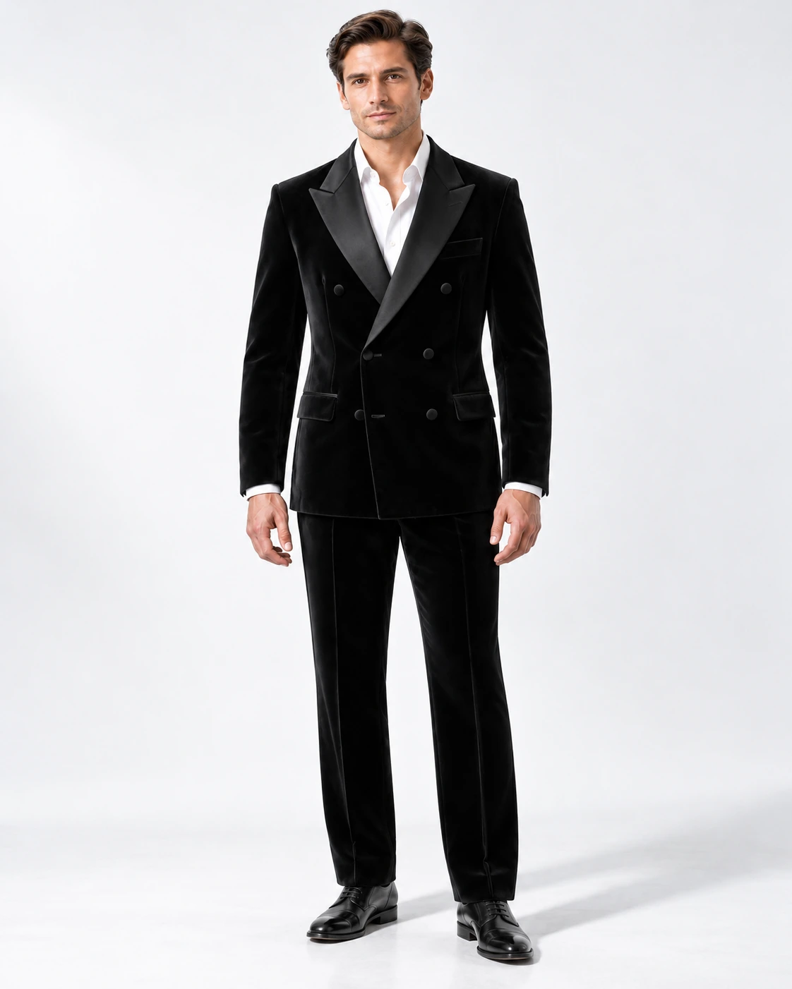 Man wearing a black velvet double-breasted tuxedo with black satin peak lapels and collar, full-length against a white studio background.