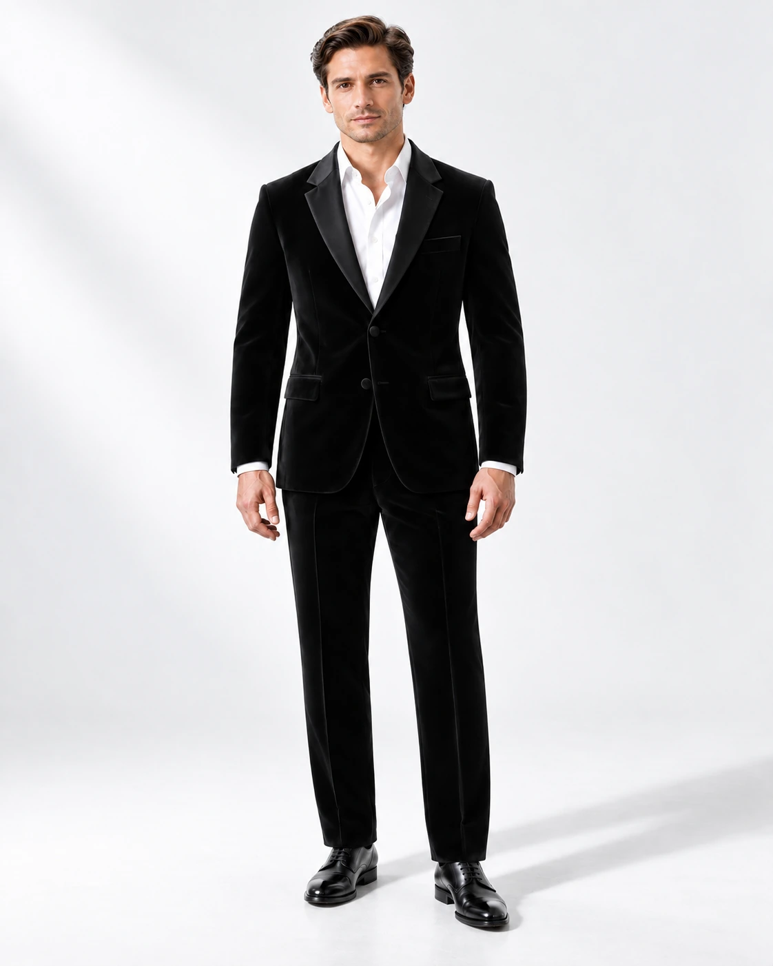 Man wearing a black velvet single-breasted tuxedo with black satin notch lapels and collar, full-length against a white studio background.
