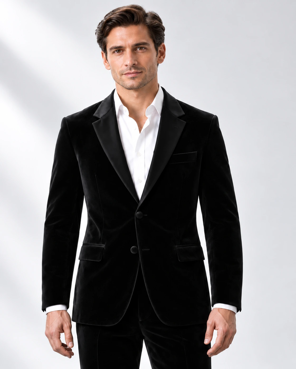 Man wearing a black velvet single-breasted tuxedo with black satin notch lapels and collar, head-to-upper-thigh portrait against a white studio background.