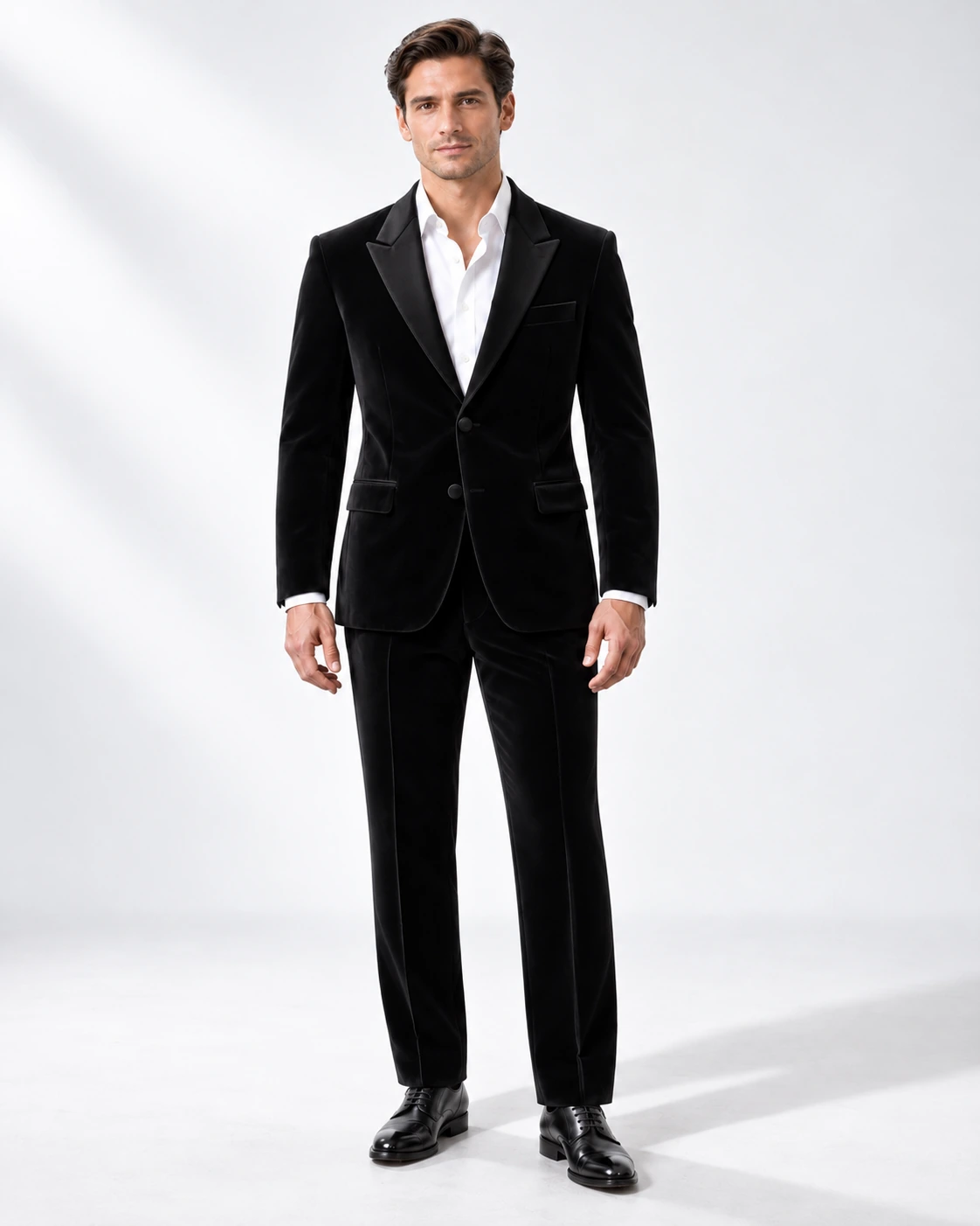 Man wearing a black velvet single-breasted tuxedo with black satin peak lapels and collar, full-length against a white studio background.