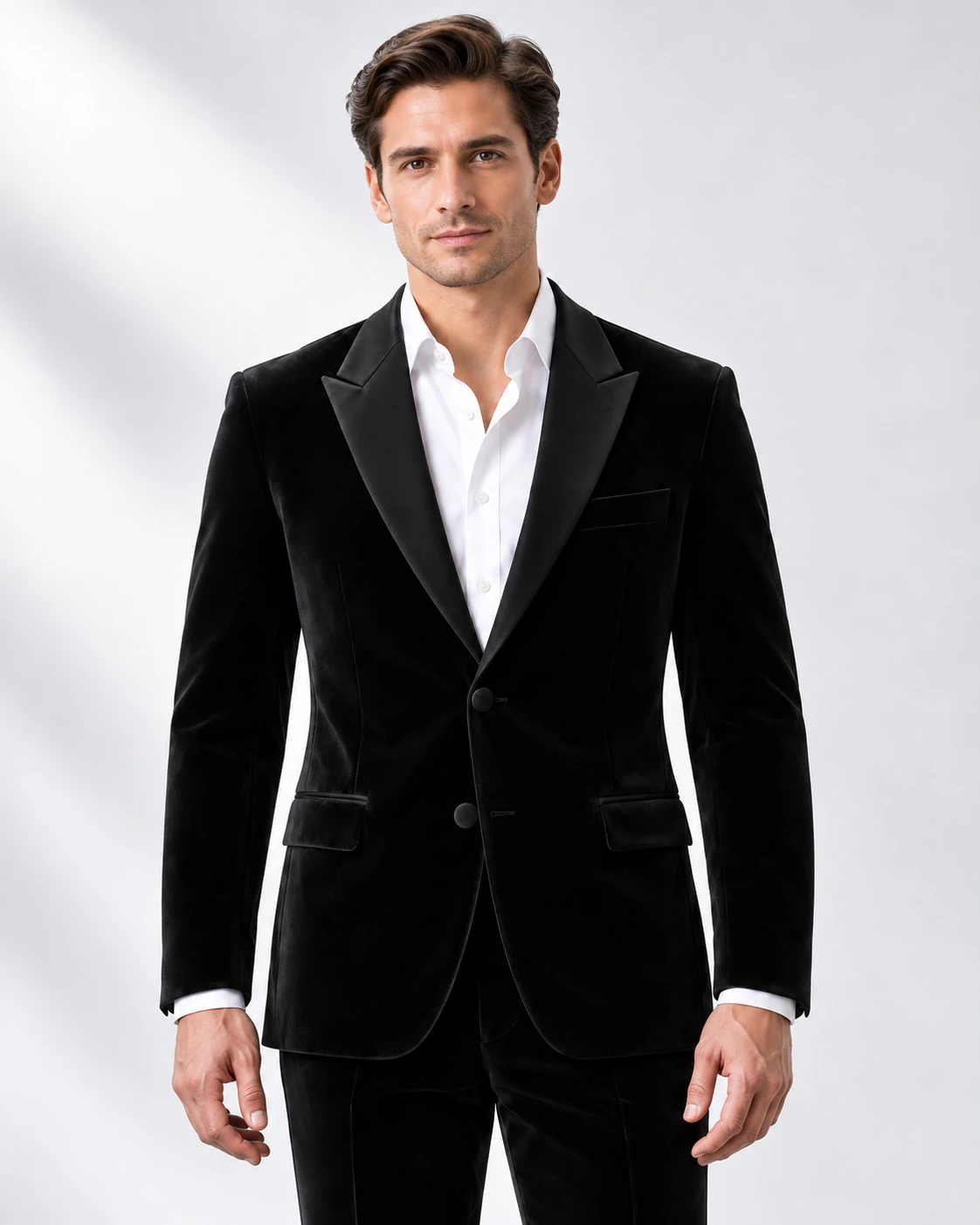 Man wearing a black velvet single-breasted tuxedo with black satin peak lapels and collar, head-to-upper-thigh portrait against a white studio background.