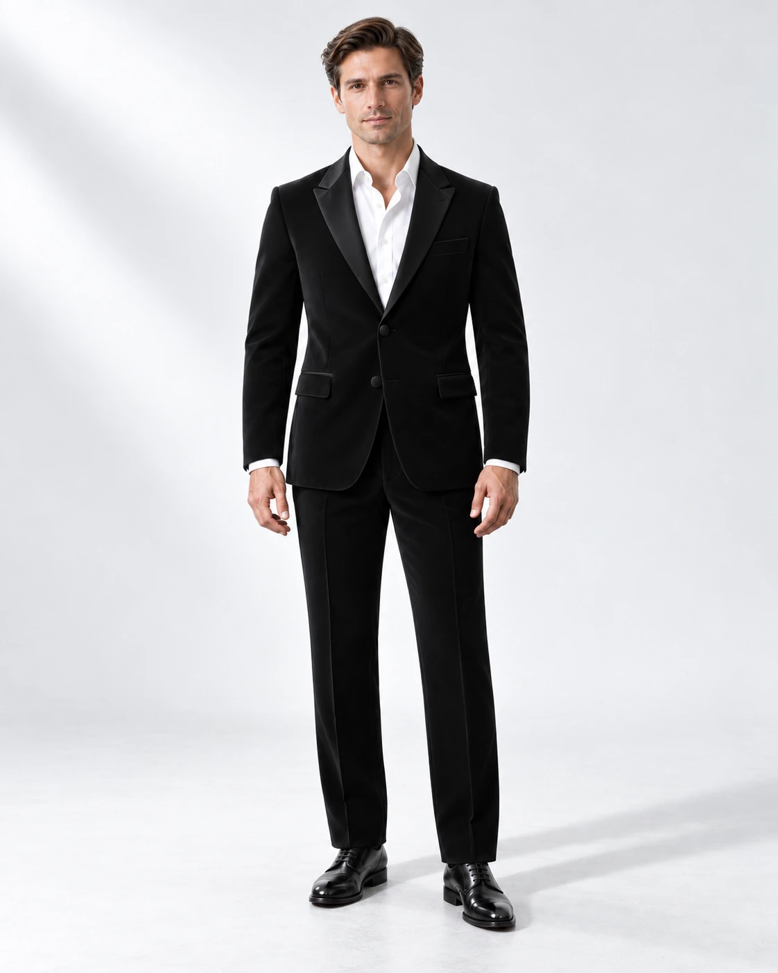 Man wearing a classic black wool single-breasted tuxedo with black satin peak lapels and collar, full-length against a white studio background.