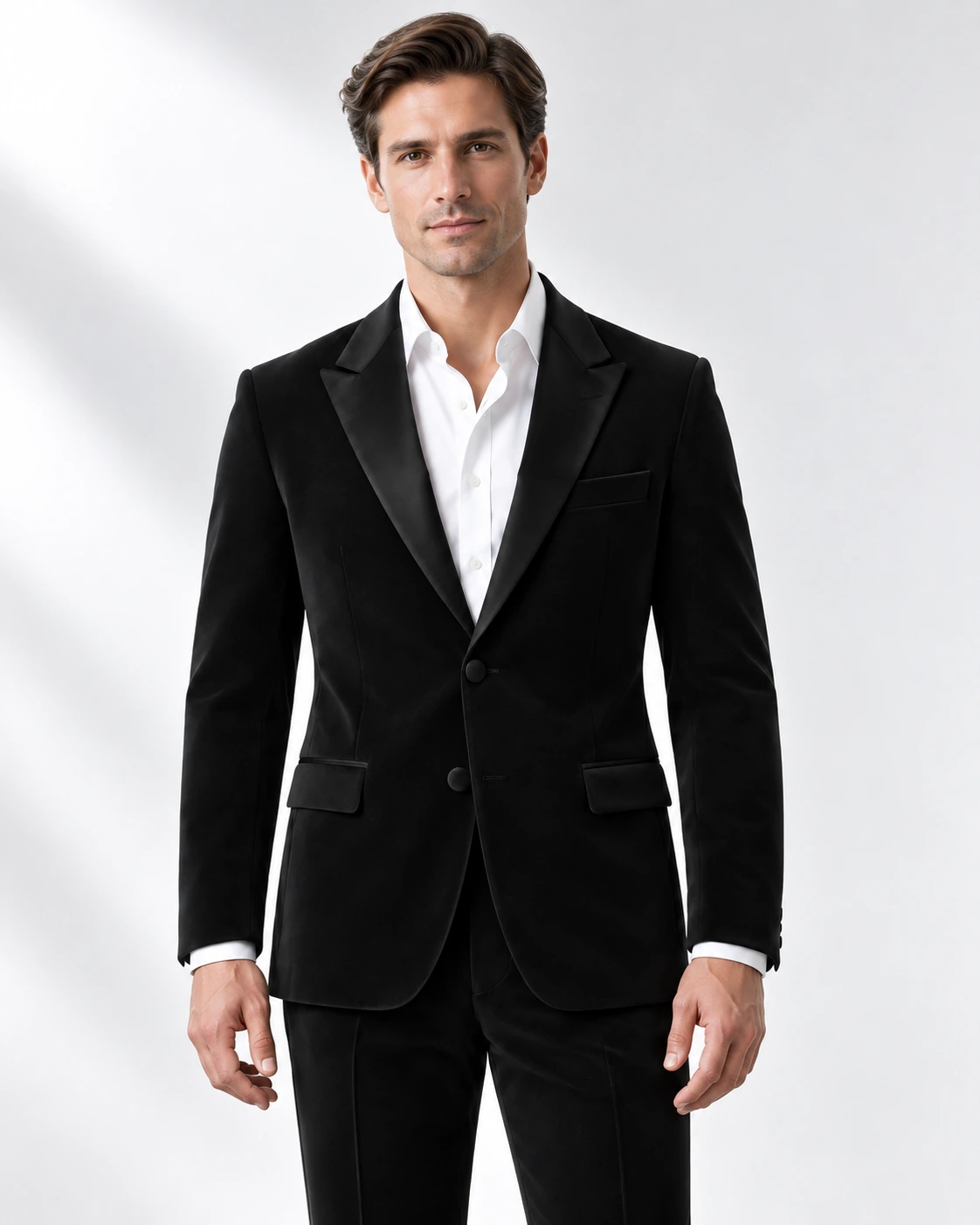 Man wearing a classic black wool single-breasted tuxedo with black satin peak lapels and collar, head-to-upper-thigh portrait against a white studio background.