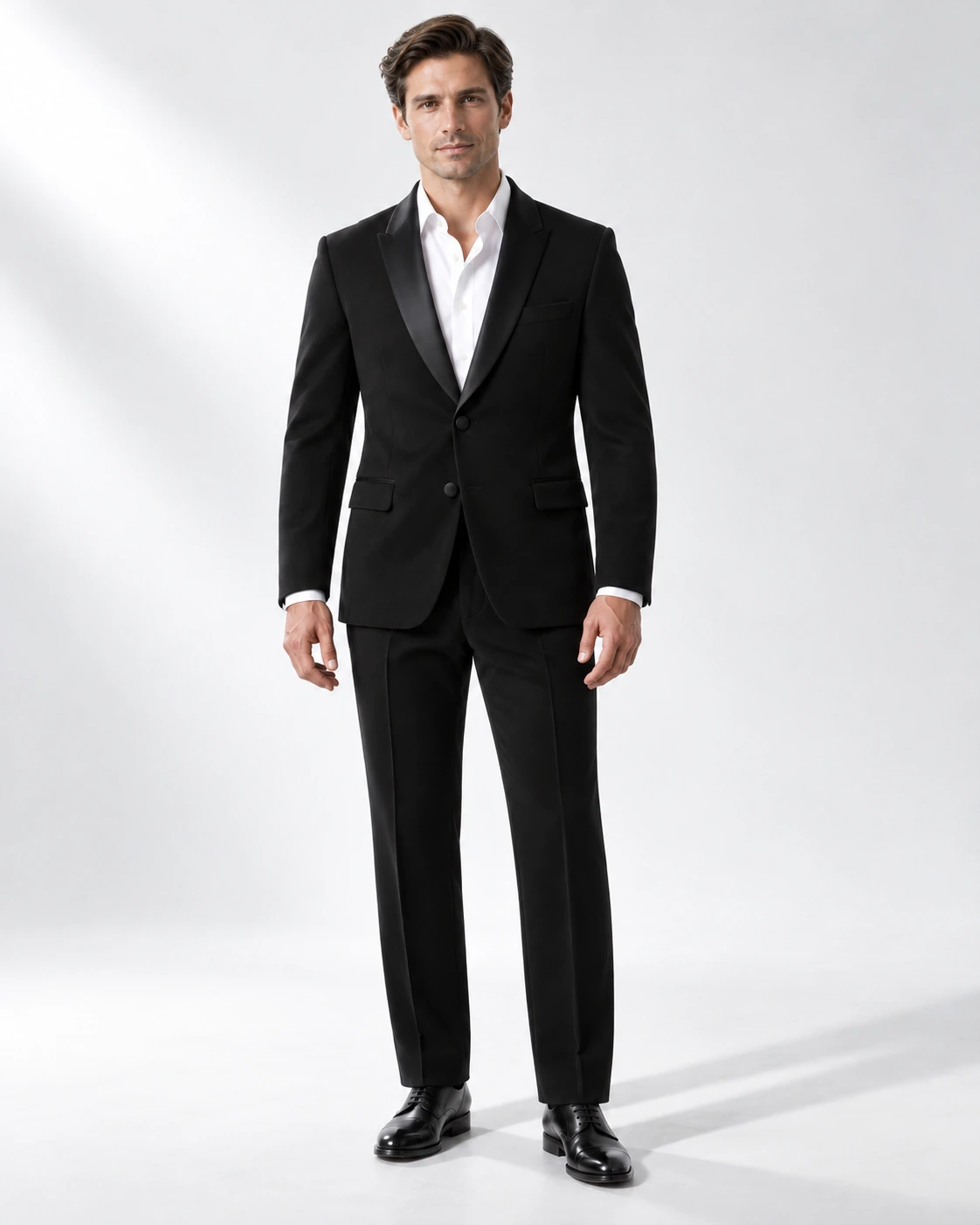 Man wearing a classic black wool single-breasted tuxedo with black satin shawl collar, full-length against a white studio background.
