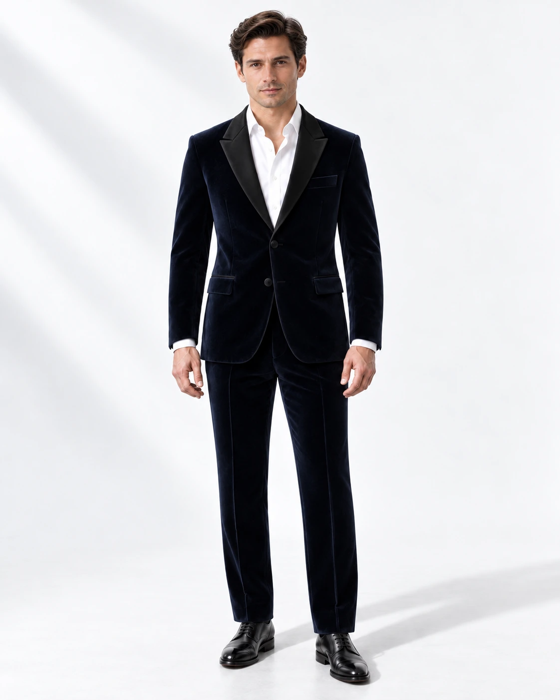 Man wearing a navy velvet single-breasted tuxedo with black satin notch lapels and collar, full-length against a white studio background.
