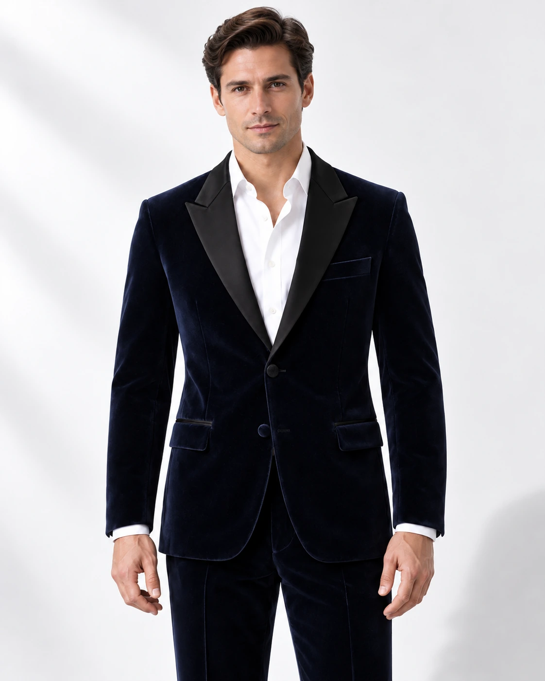 Man wearing a navy velvet single-breasted tuxedo with black satin peak lapels and collar, head-to-upper-thigh portrait against a white studio background.