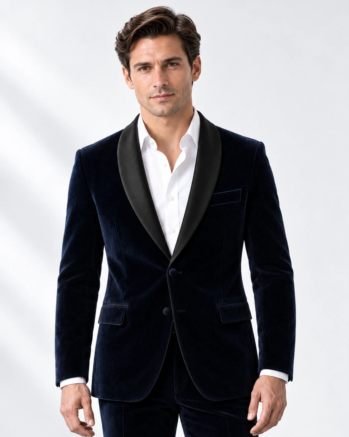 Man wearing a navy velvet single-breasted tuxedo with black satin shawl collar, head-to-upper-thigh portrait against a white studio background.