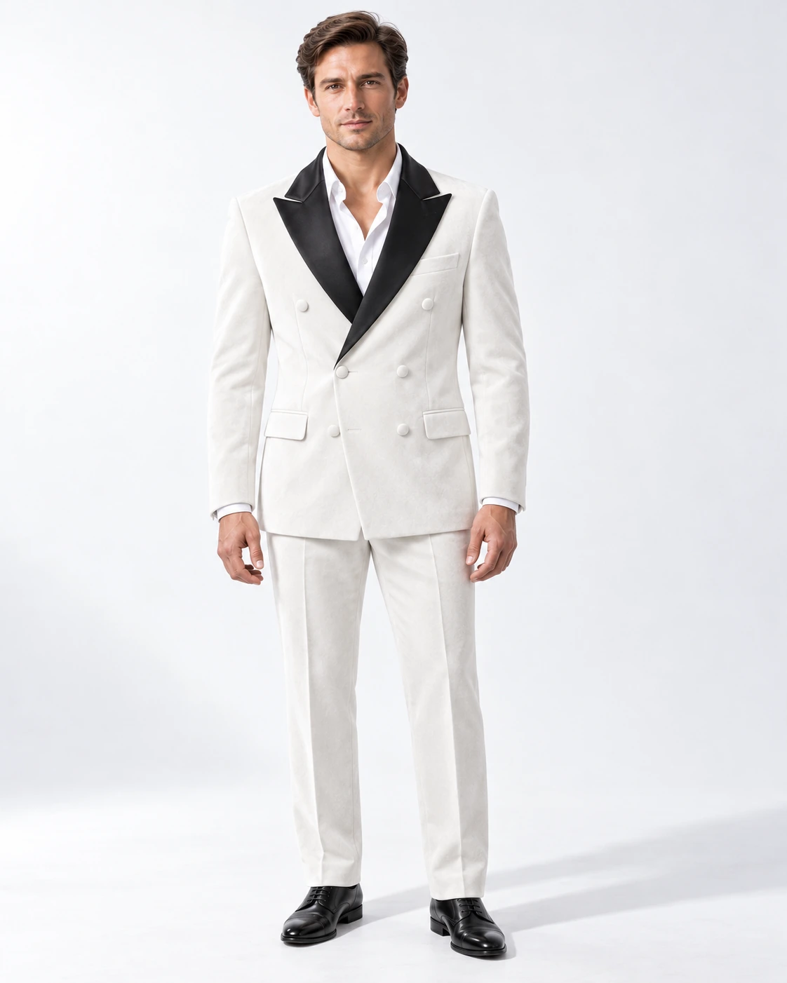 Man wearing a white velvet double-breasted tuxedo with black satin peak lapels and collar, full-length against a white studio background.