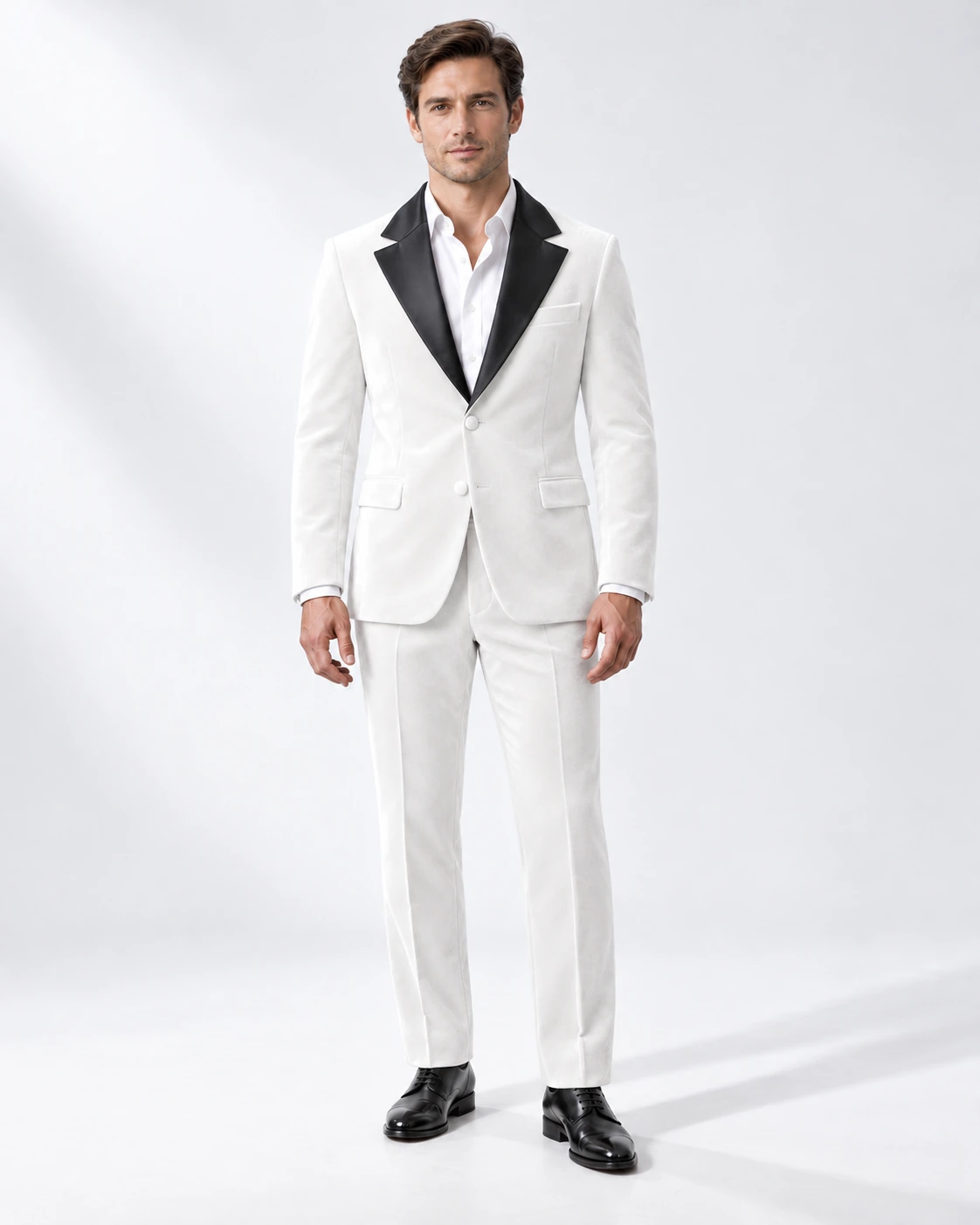 Man wearing a white velvet single-breasted tuxedo with black satin notch lapels and collar, full-length against a white studio background.