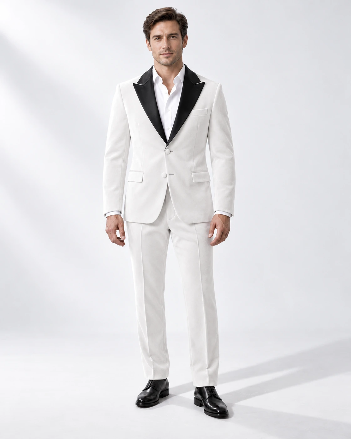 Man wearing a white velvet single-breasted tuxedo with black satin peak lapels and collar, full-length against a white studio background.