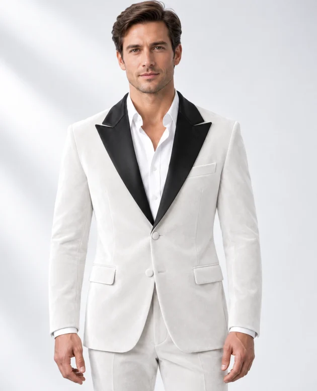 Man wearing a white velvet single-breasted tuxedo with black satin peak lapels and collar, head-to-upper-thigh portrait against a white studio background.