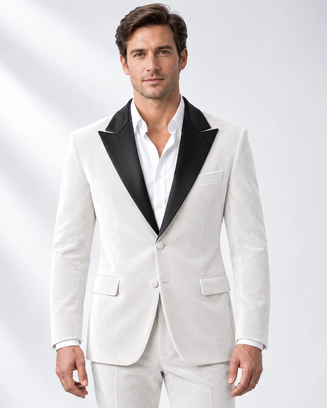 Man wearing a white velvet single-breasted tuxedo with black satin peak lapels and collar, head-to-upper-thigh portrait against a white studio background.