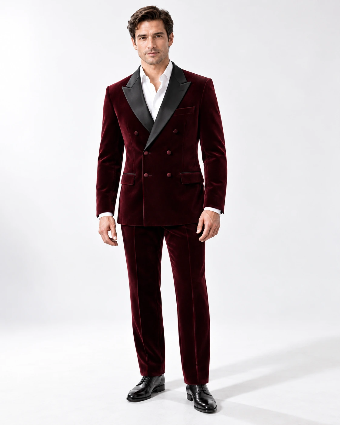 Man wearing a wine velvet double-breasted tuxedo with black satin peak lapels and collar, full-length against a white studio background.