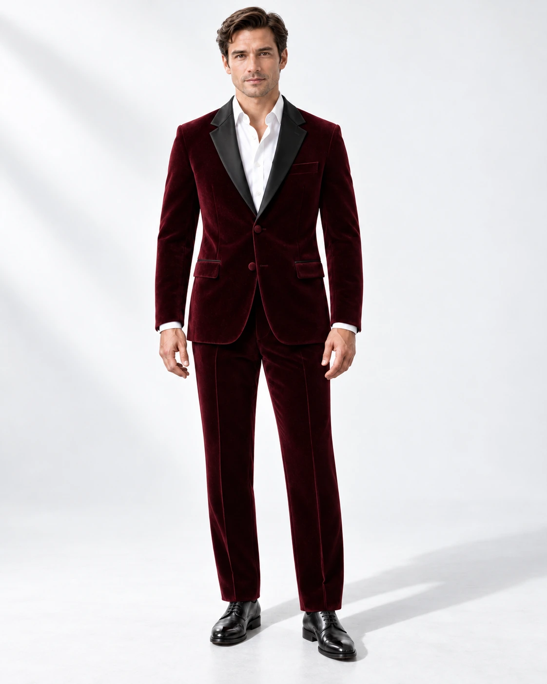 Man wearing a wine velvet single-breasted tuxedo with black satin notch lapels and collar, full-length against a white studio background.