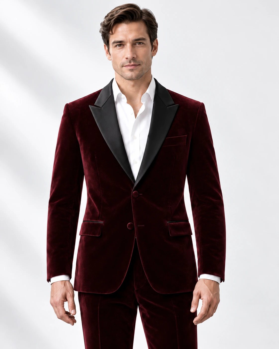 Man wearing a wine velvet single-breasted tuxedo with black satin peak lapels and collar, head-to-upper-thigh portrait against a white studio background.