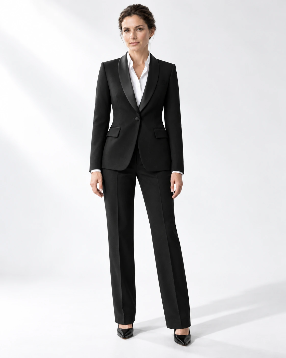Woman wearing a classic black wool single-breasted tuxedo with black satin shawl collar, full-length against a white studio background.