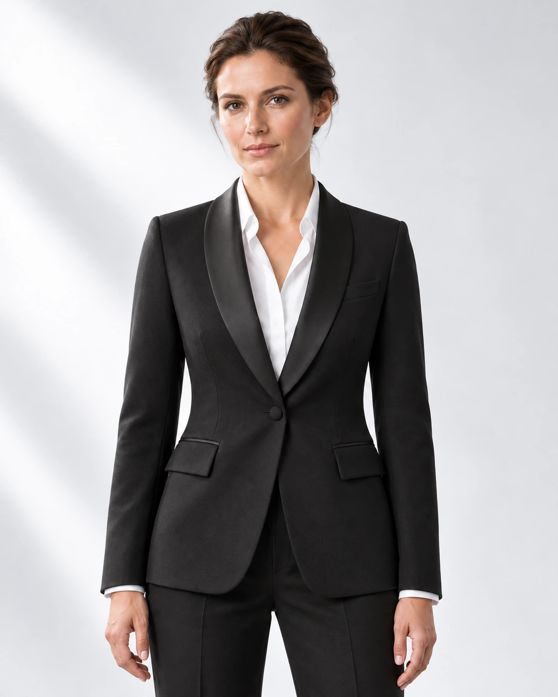 Woman wearing a classic black wool single-breasted tuxedo with black satin shawl collar, head-to-upper-thigh portrait against a white studio background.