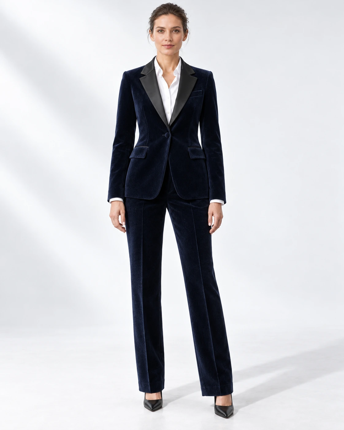 Woman wearing a navy velvet single-breasted tuxedo with black satin notch lapels and collar, full-length against a white studio background.