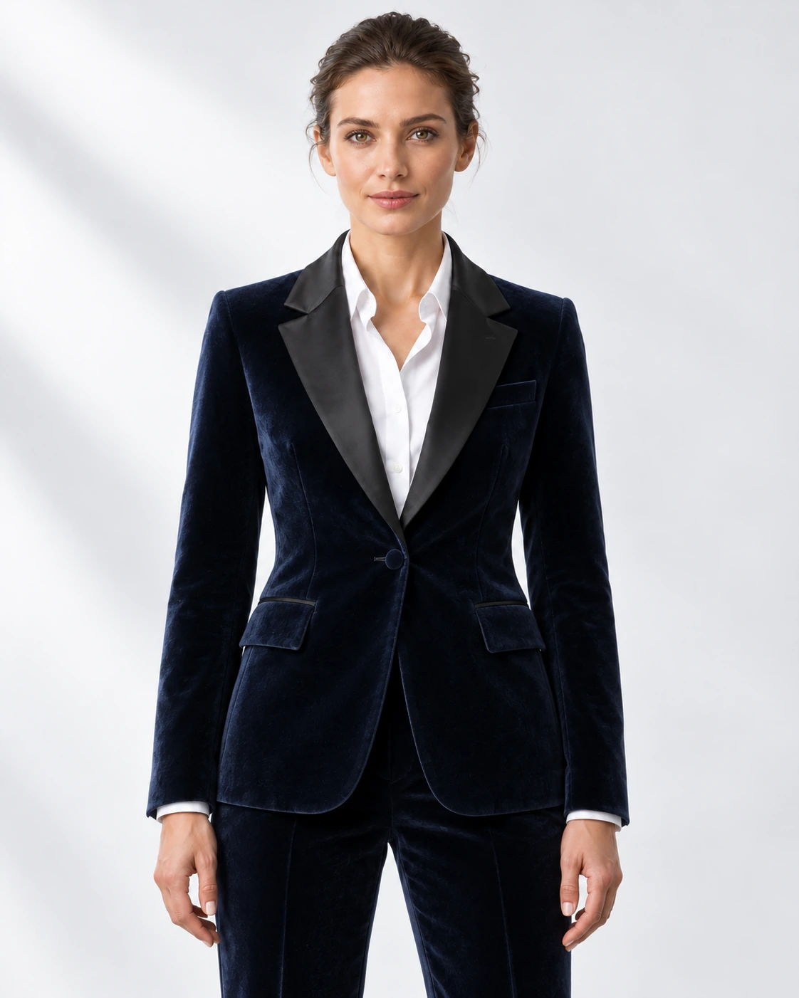 Woman wearing a navy velvet single-breasted tuxedo with black satin notch lapels and collar, head-to-upper-thigh portrait against a white studio background.