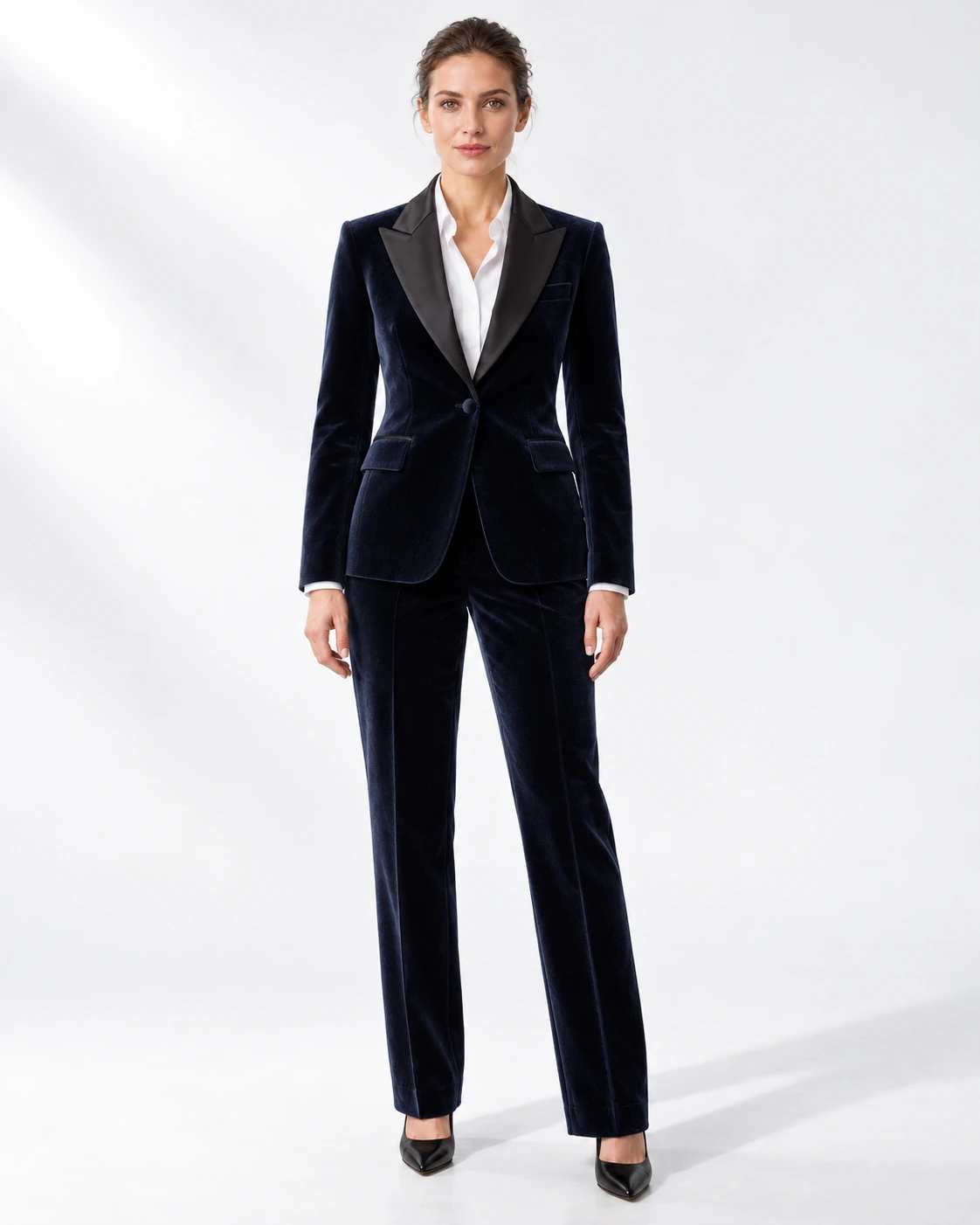 Woman wearing a navy velvet single-breasted tuxedo with black satin peak lapels and collar, full-length against a white studio background.