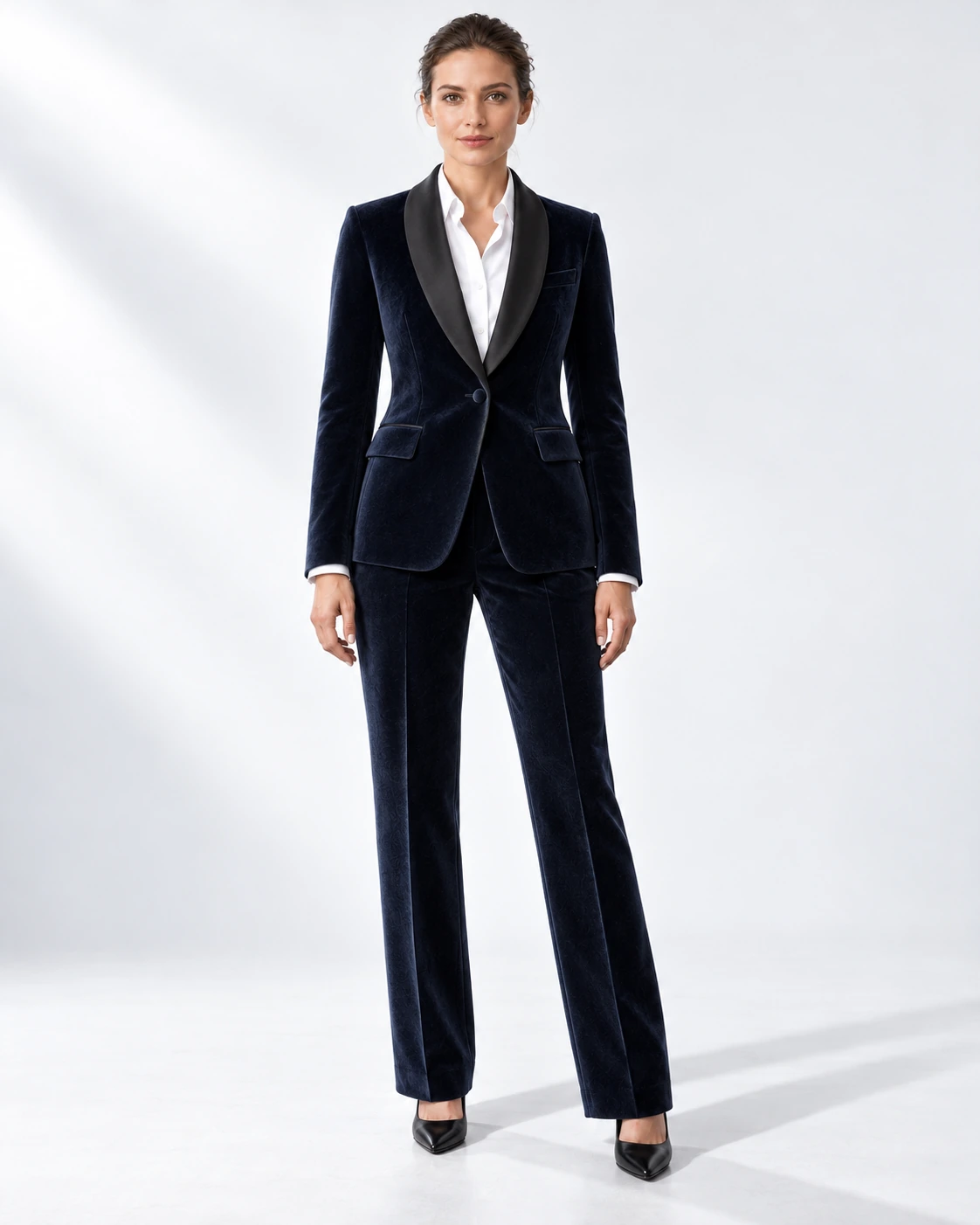 Woman wearing a navy velvet single-breasted tuxedo with black satin shawl collar, full-length against a white studio background.