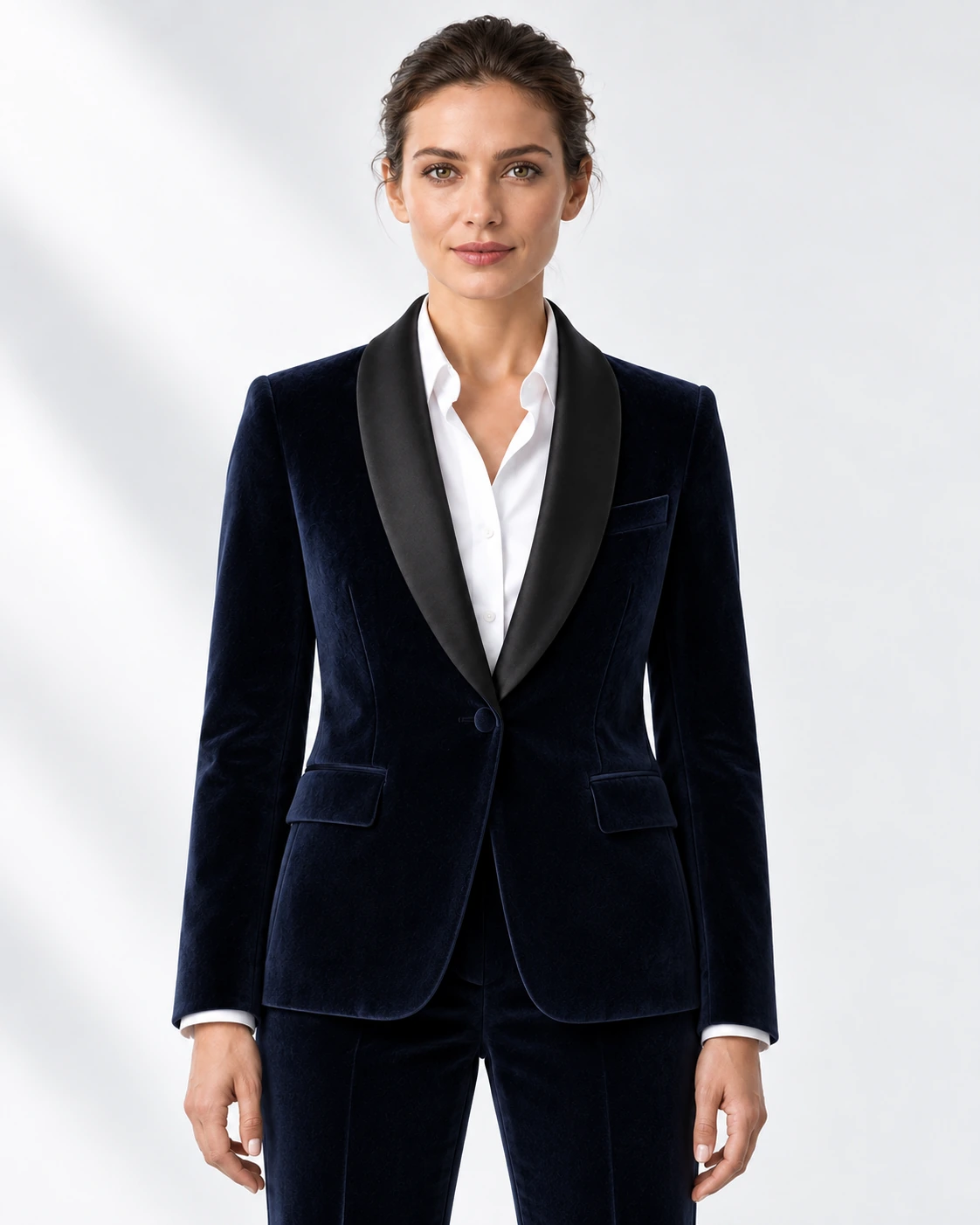 Woman wearing a navy velvet single-breasted tuxedo with black satin shawl collar, head-to-upper-thigh portrait against a white studio background.