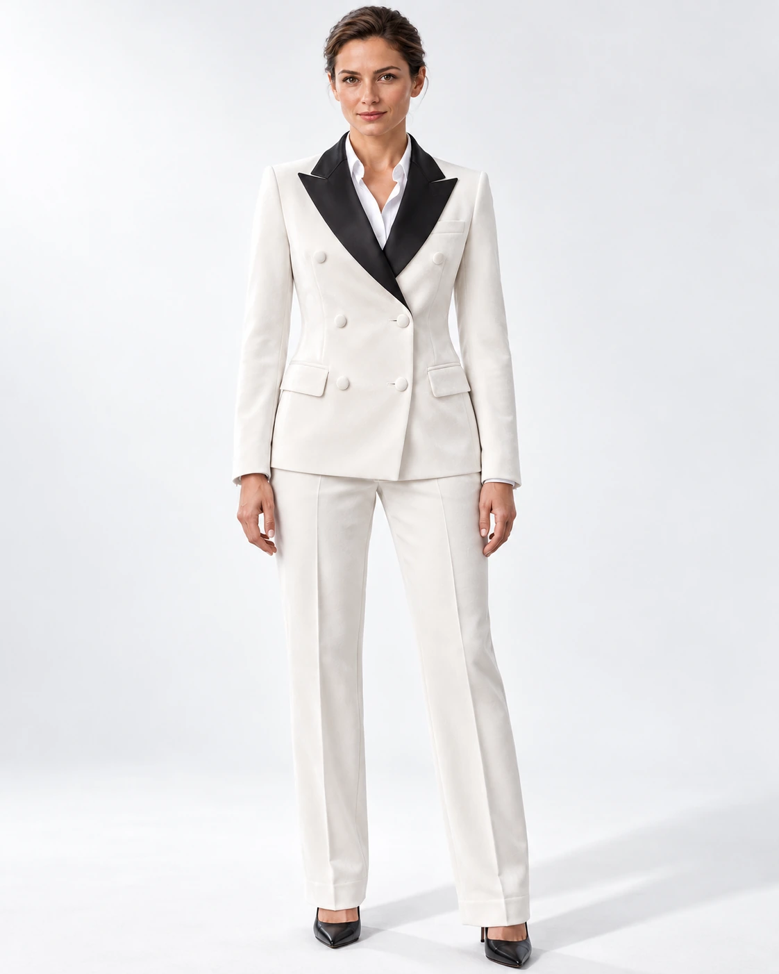 Woman wearing a white velvet double-breasted tuxedo with black satin peak lapels and collar, full-length against a white studio background.