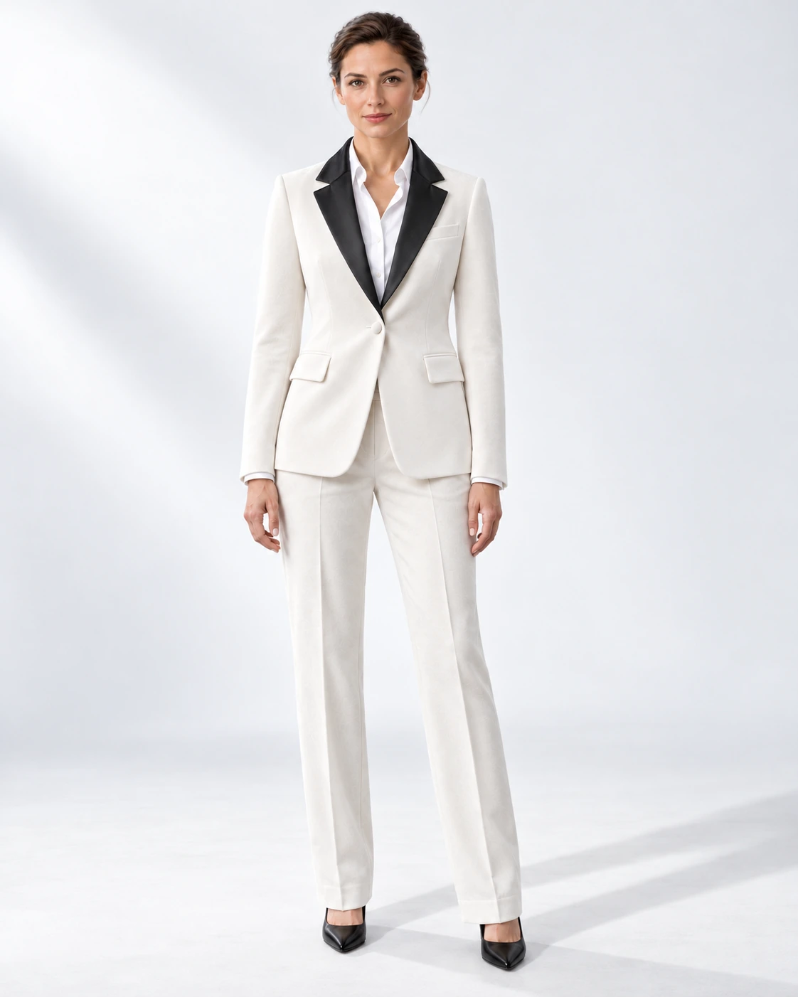 Woman wearing a white velvet single-breasted tuxedo with black satin notch lapels and collar, full-length against a white studio background.