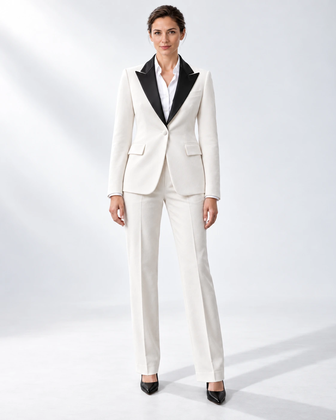 Woman wearing a white velvet single-breasted tuxedo with black satin peak lapels and collar, full-length against a white studio background.