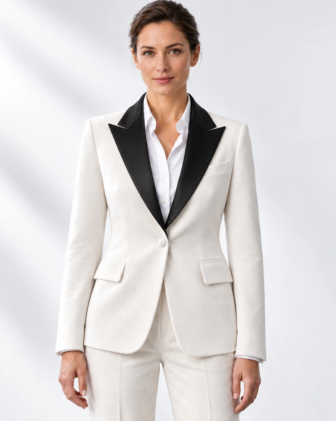 Woman wearing a white velvet single-breasted tuxedo with black satin peak lapels and collar, head-to-upper-thigh portrait against a white studio background.