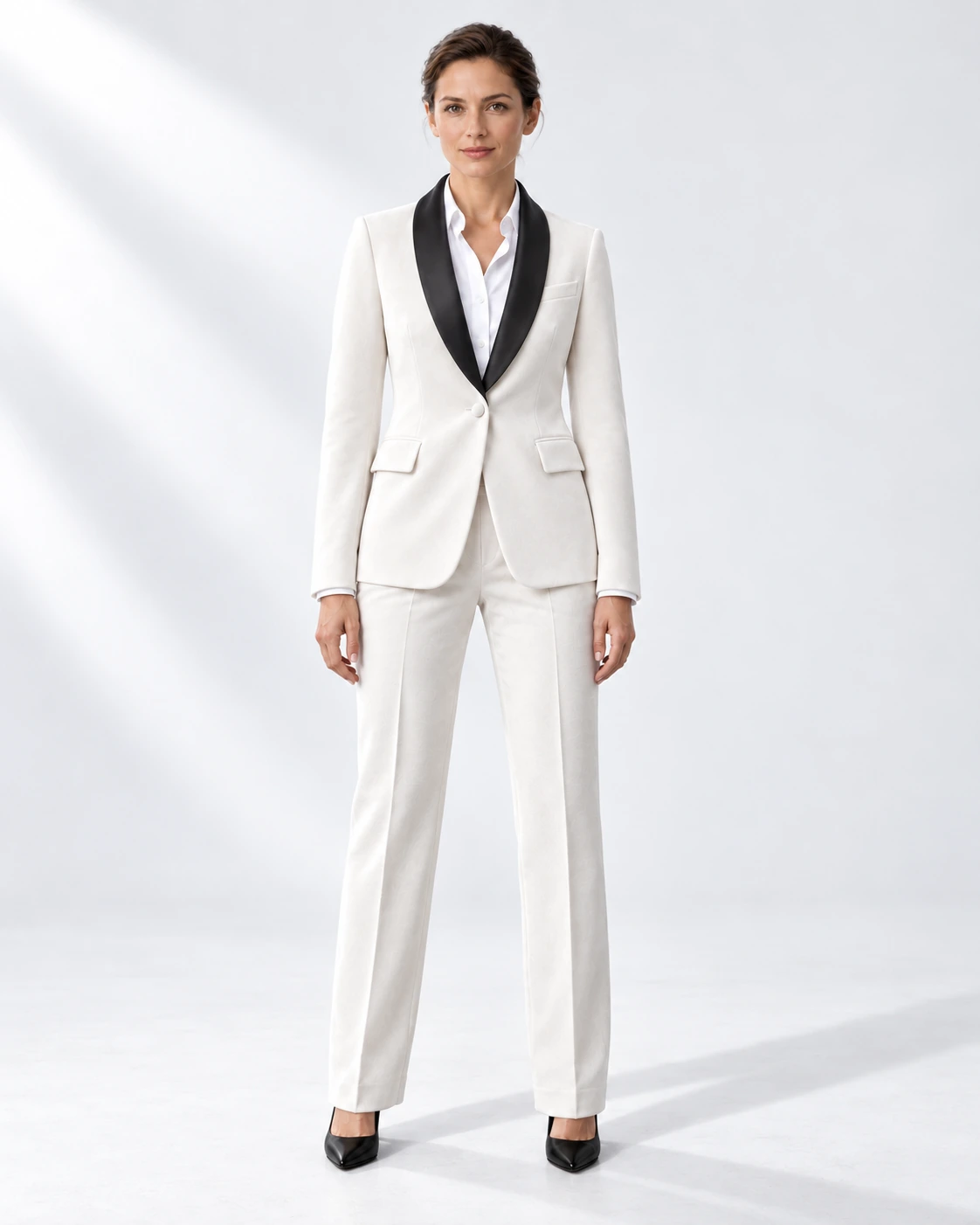 Woman wearing a white velvet single-breasted tuxedo with black satin shawl collar, full-length against a white studio background.