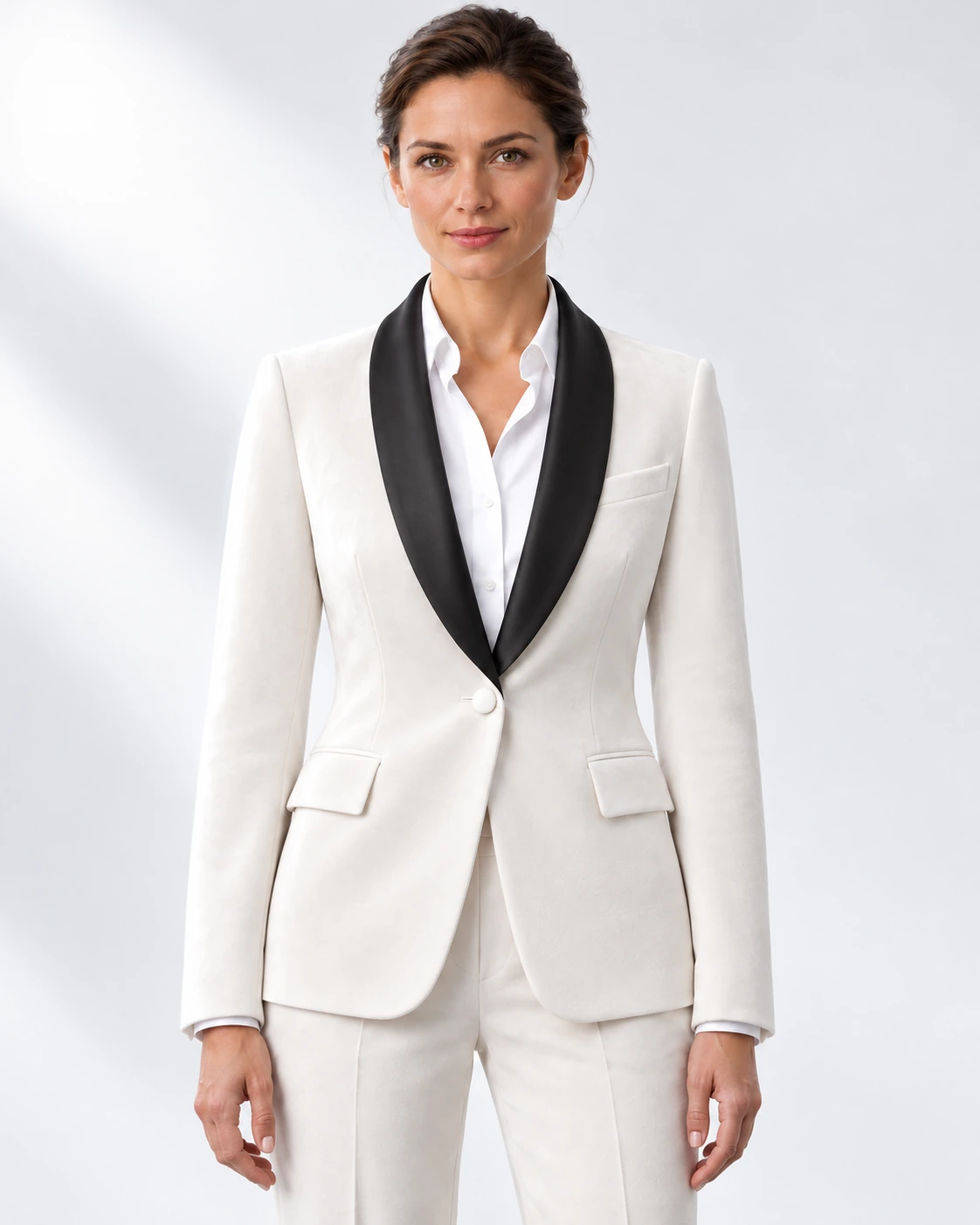 Woman wearing a white velvet single-breasted tuxedo with black satin shawl collar, head-to-upper-thigh portrait against a white studio background.