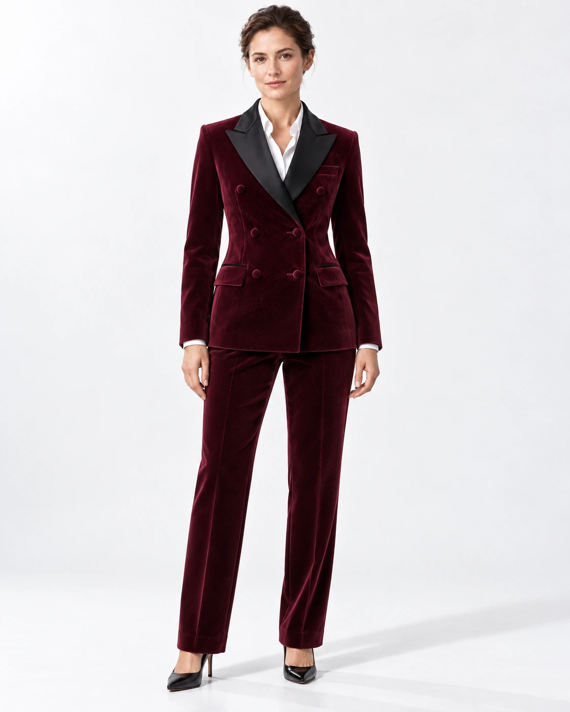 Woman wearing a wine velvet double-breasted tuxedo with black satin peak lapels and collar, full-length against a white studio background.