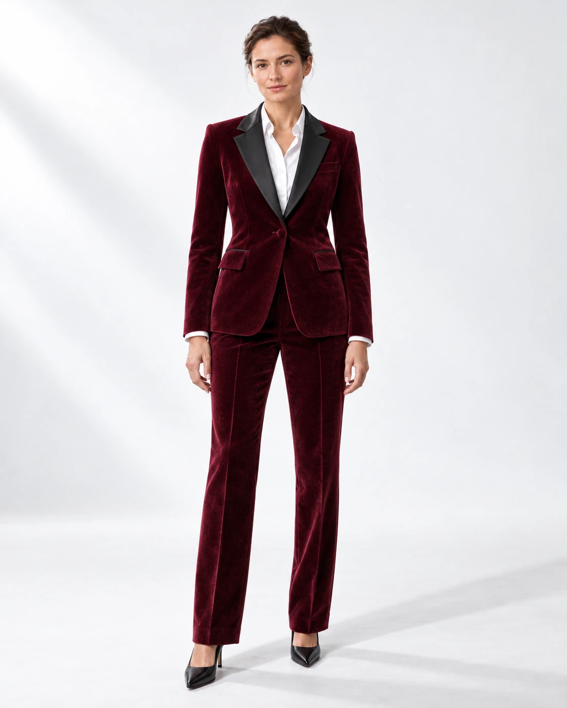 Woman wearing a wine velvet single-breasted tuxedo with black satin notch lapels and collar, full-length against a white studio background.