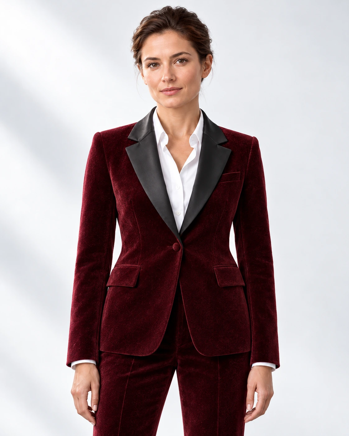 Woman wearing a wine velvet single-breasted tuxedo with black satin notch lapels and collar, head-to-upper-thigh portrait against a white studio background.