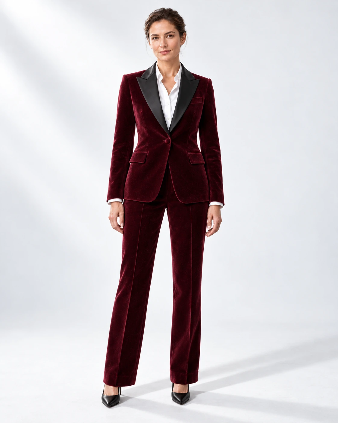 Woman wearing a wine velvet single-breasted tuxedo with black satin peak lapels and collar, full-length against a white studio background.