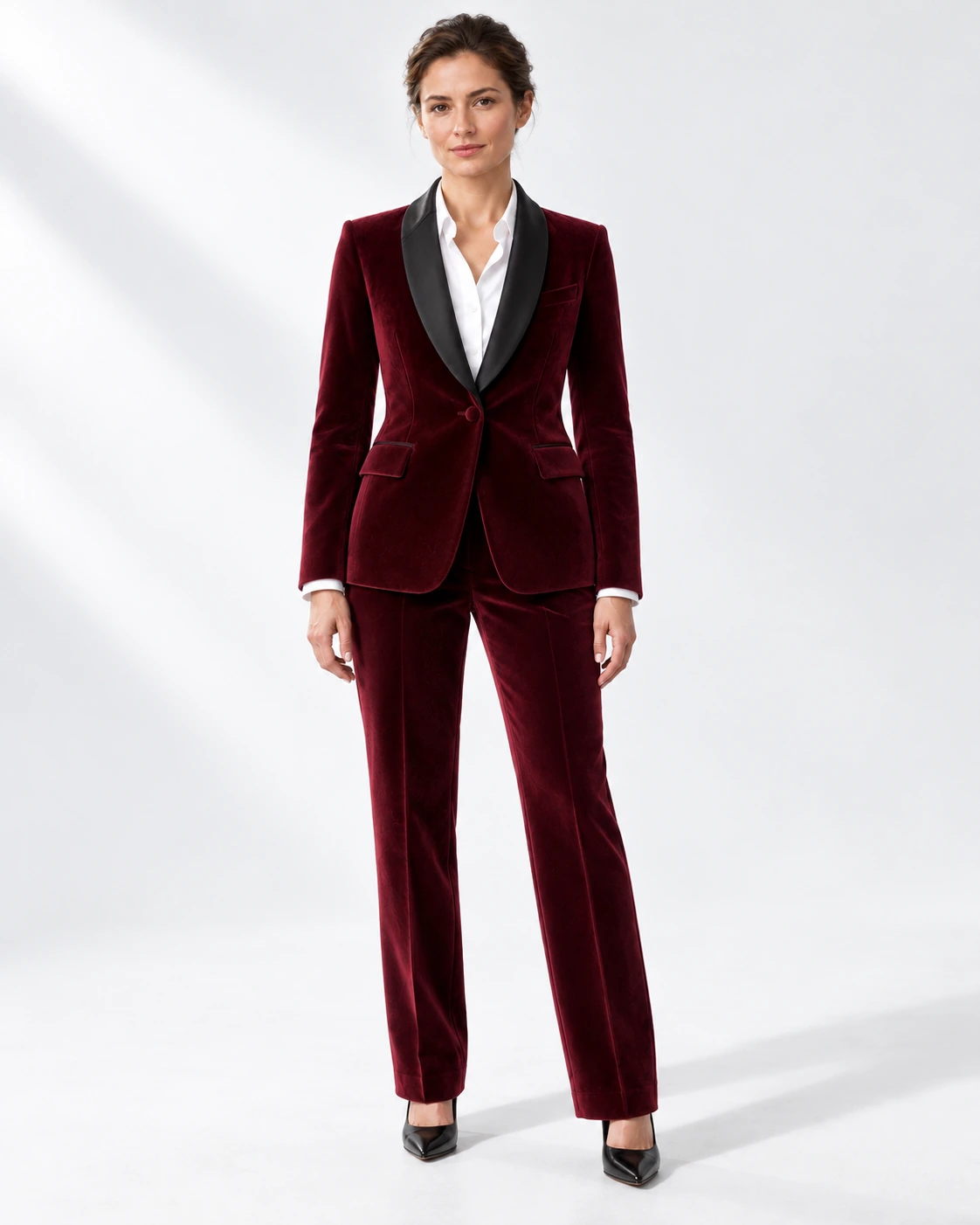 Woman wearing a wine velvet single-breasted tuxedo with black satin shawl collar, full-length against a white studio background.