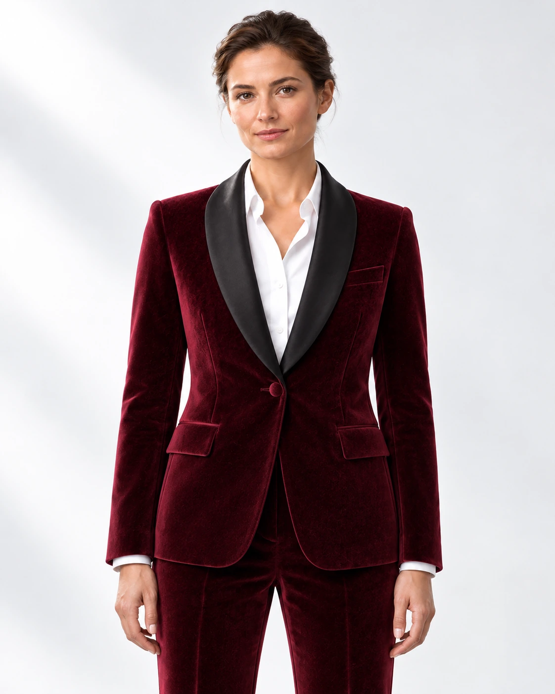 Woman wearing a wine velvet single-breasted tuxedo with black satin shawl collar, head-to-upper-thigh portrait against a white studio background.